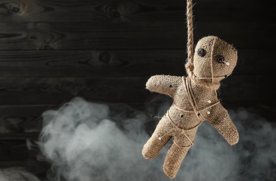 Voodoo doll with pins and smoke on dark wooden background. Space for text