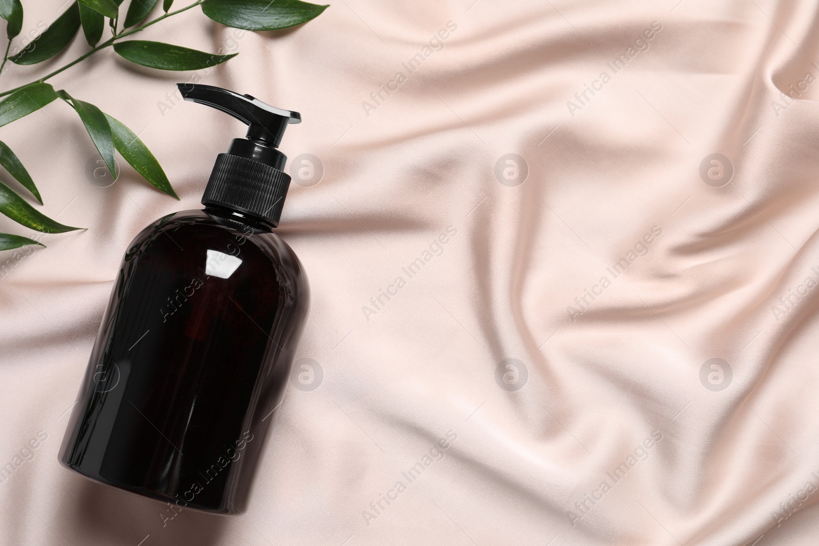Photo of Bottle of cosmetic product and leaves on pink fabric, flat lay. Space for text