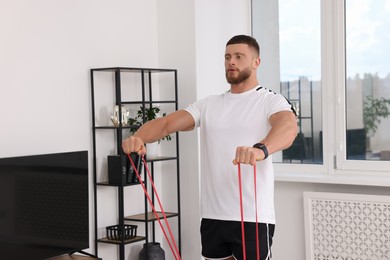Photo of Athletic man doing exercise with elastic resistance band at home