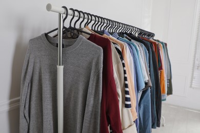 Rack with stylish clothes near white wall indoors. Fast fashion
