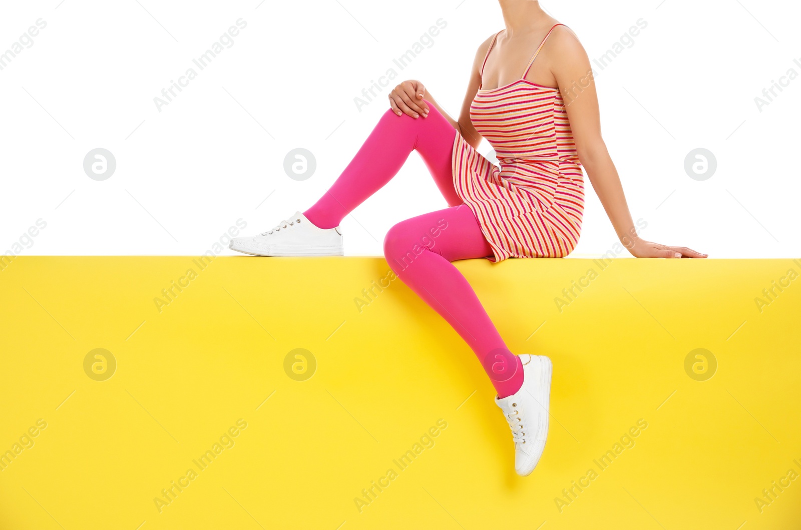 Photo of Woman wearing pink tights sitting on yellow background, closeup