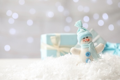 Photo of Snowman toy on snow against blurred festive lights, space for text. Christmas decoration