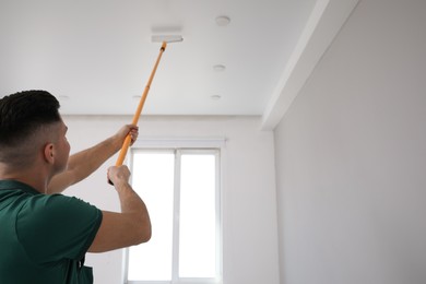 Man painting ceiling with roller in room. Space for text