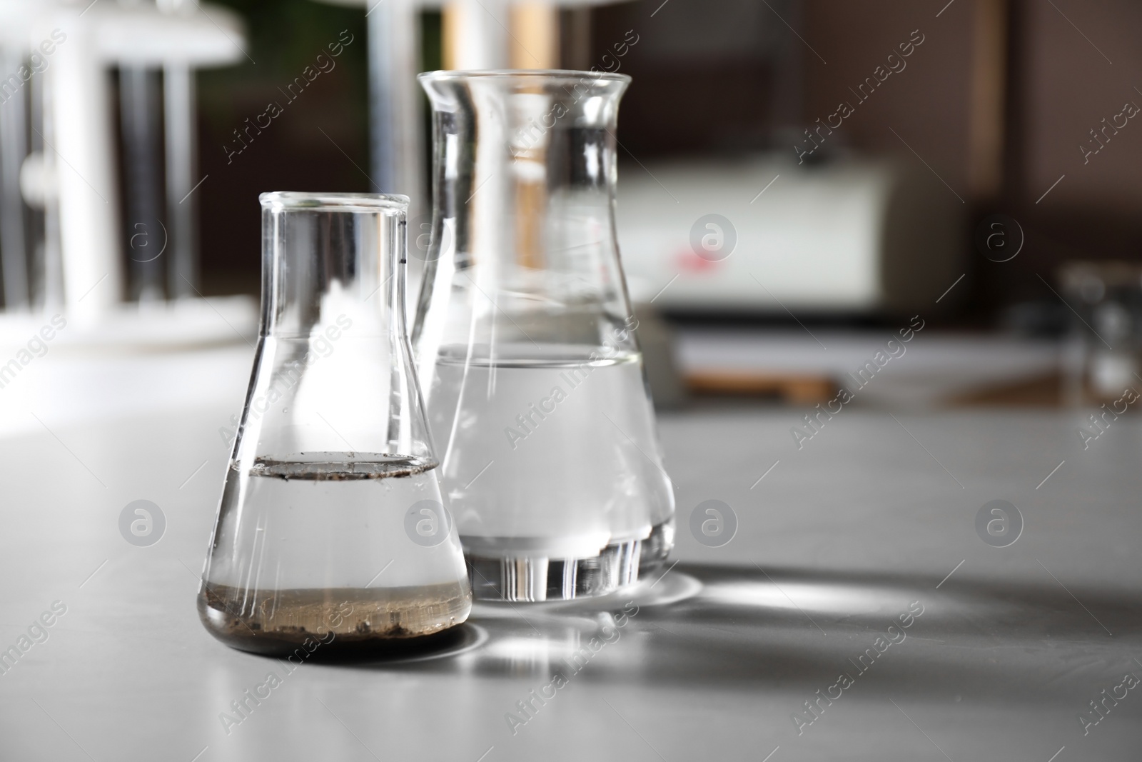 Photo of Glassware with soil extract and water on grey table, space for text. Laboratory research