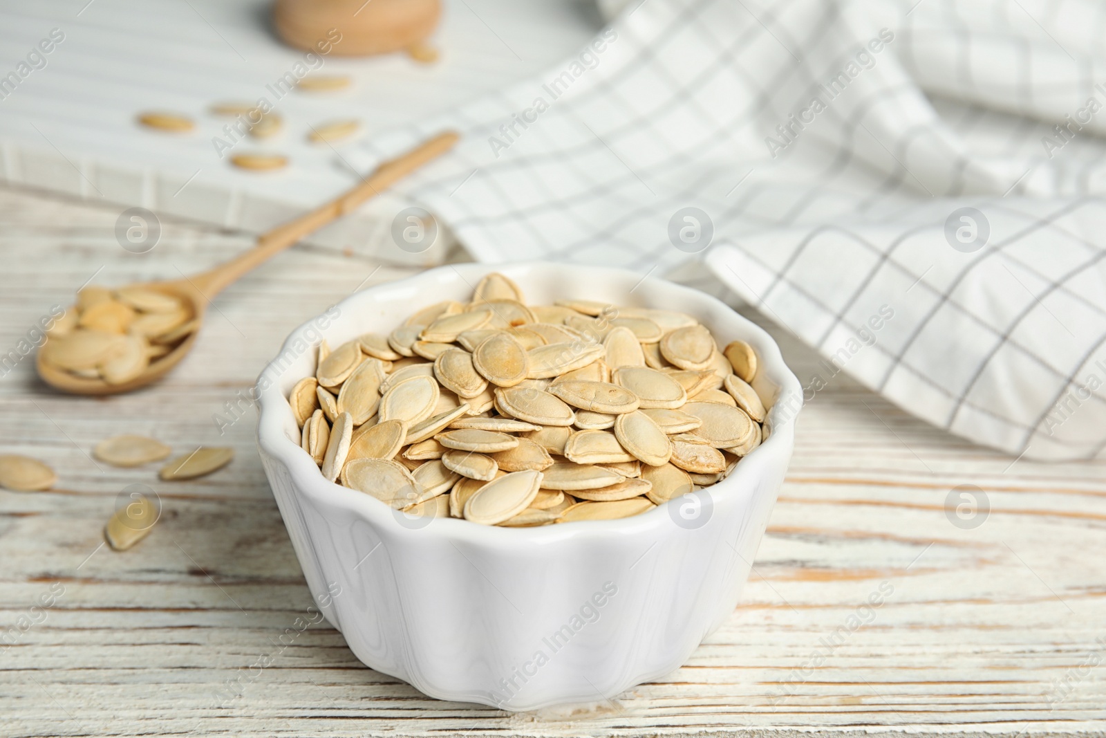 Photo of Bowl of raw pumpkin seeds on white wooden table