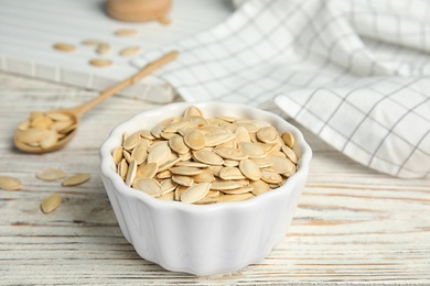 Photo of Bowl of raw pumpkin seeds on white wooden table