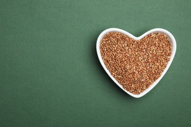 Buckwheat grains on dark green background, top view. Space for text