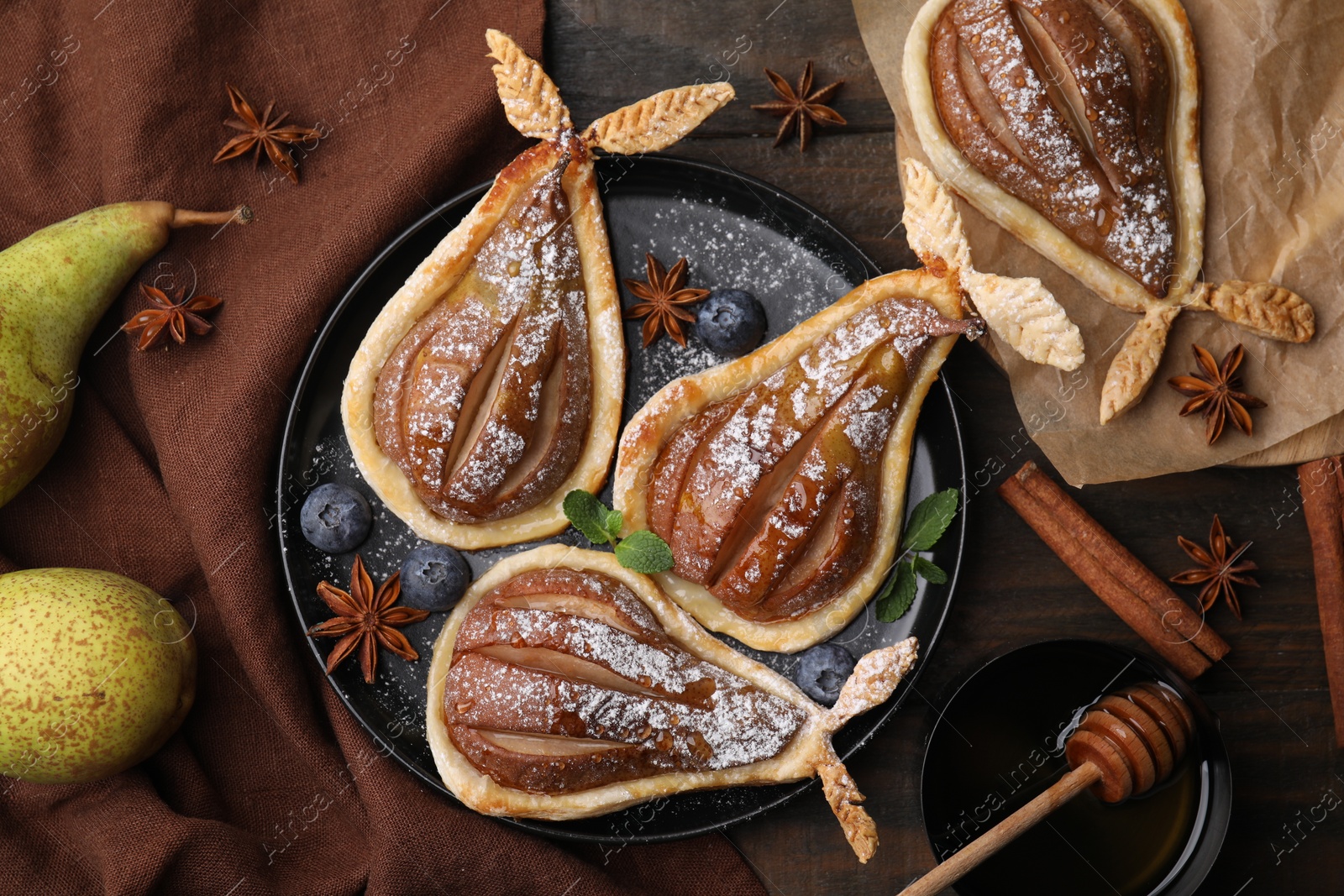 Photo of Delicious pears baked in puff pastry with powdered sugar served on wooden table, flat lay