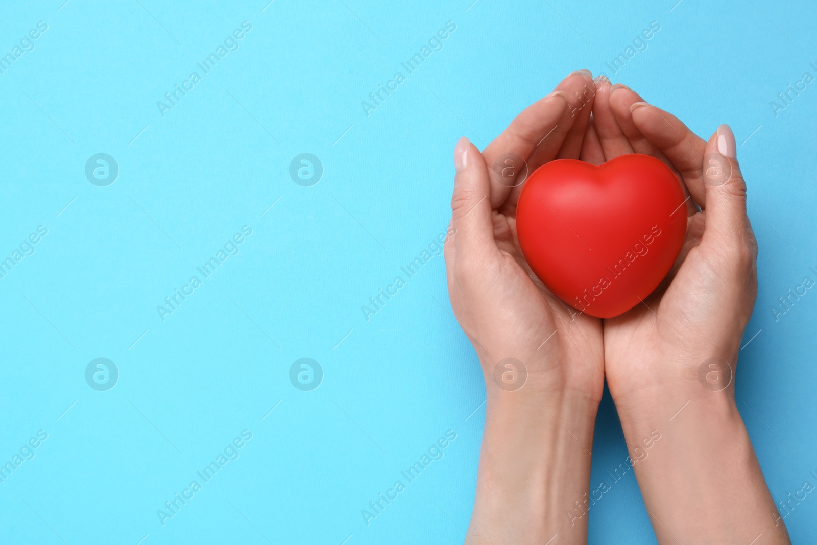 Photo of Woman holding red decorative heart on light blue background, top view and space for text. Cardiology concept
