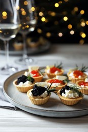Delicious tartlets with red and black caviar served on white wooden table against blurred festive lights, closeup. Space for text