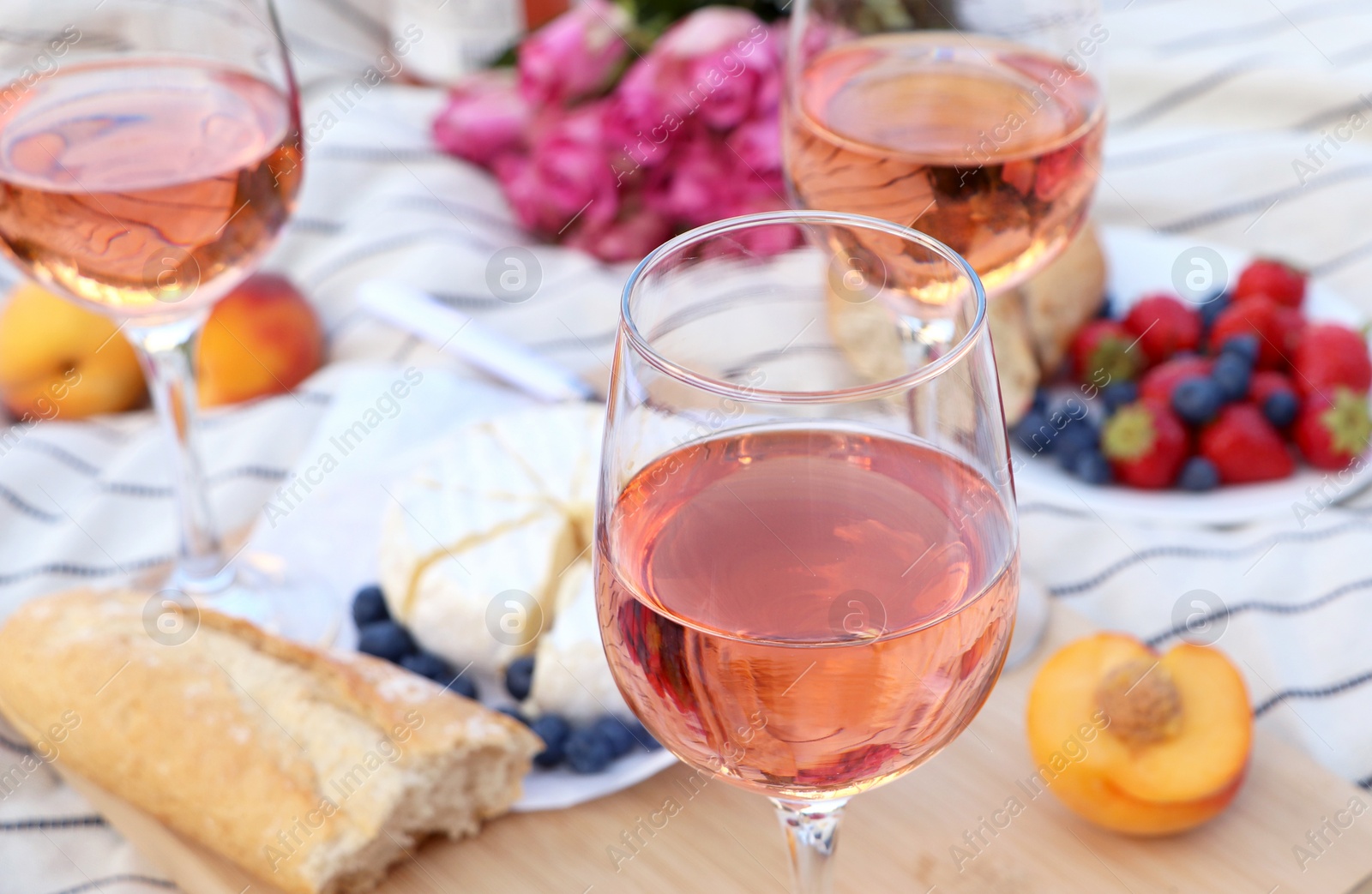 Photo of Glasses of delicious rose wine and food on white picnic blanket, closeup