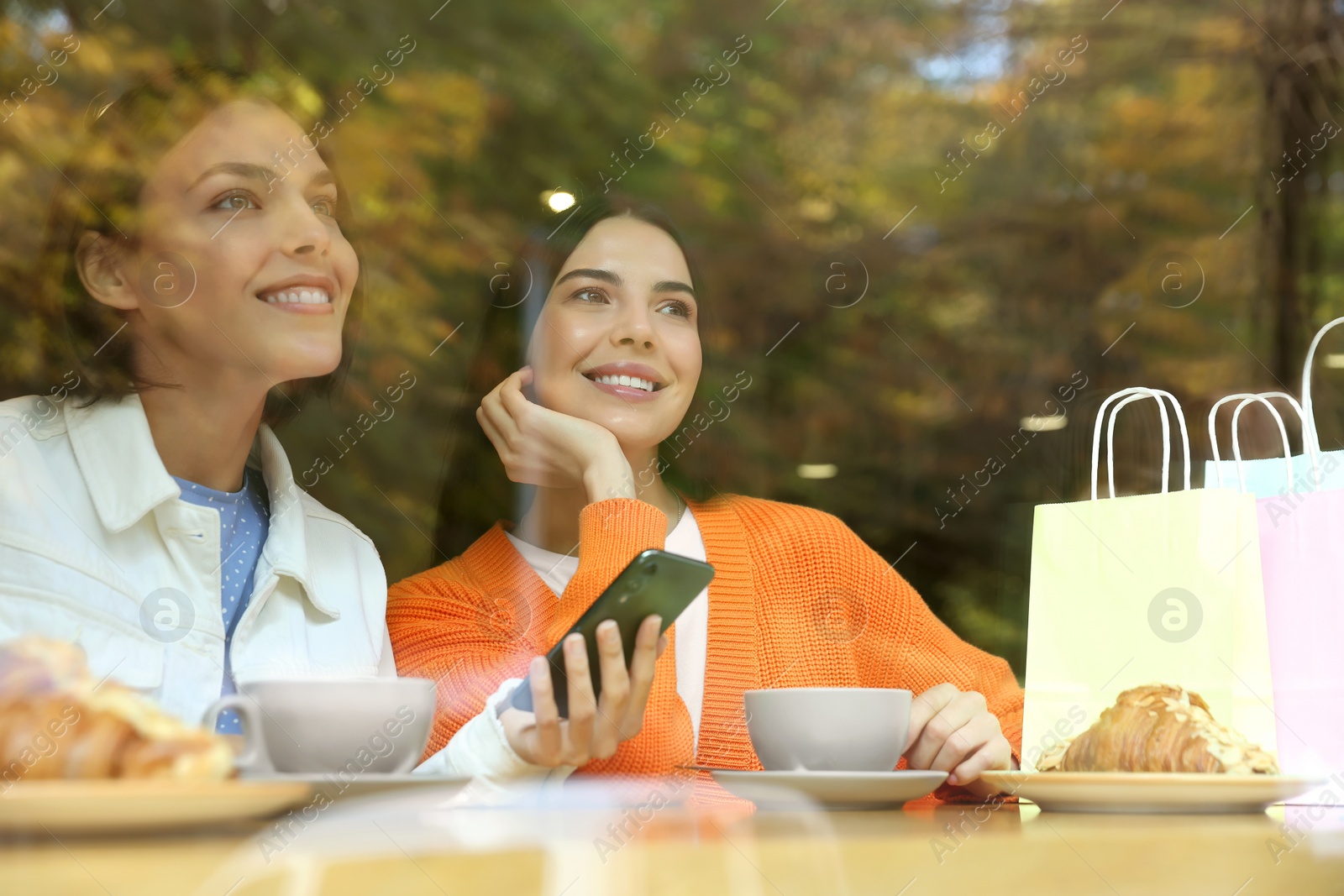 Photo of Special Promotion. Happy young women using smartphone at table in cafe, view from outdoors