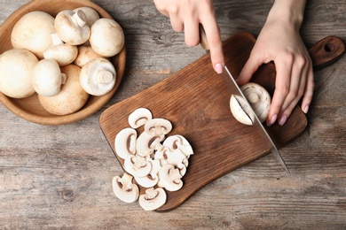 Photo of Young woman cutting fresh champignon mushrooms on wooden board, top view