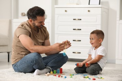 Motor skills development. Father and son playing with wooden pieces and string for threading activity on floor indoors