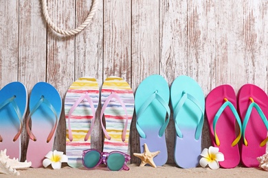 Different bright flip flops and sunglasses on sand near wooden wall, space for text. Summer beach accessories