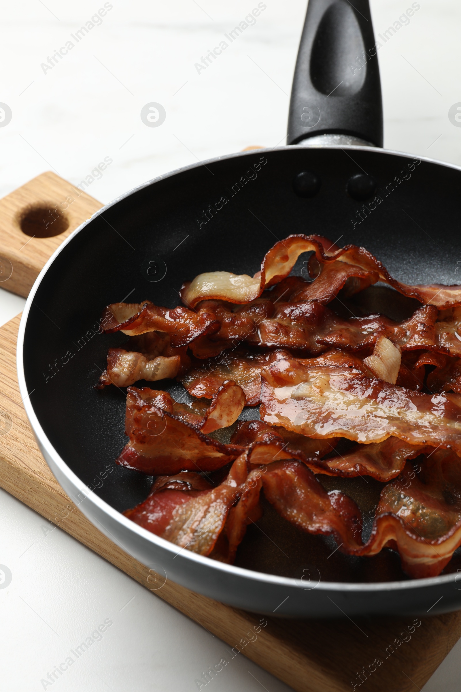 Photo of Delicious bacon slices in frying pan on white table, closeup