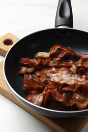 Delicious bacon slices in frying pan on white table, closeup