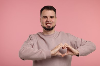 Photo of Man showing heart gesture with hands on pink background