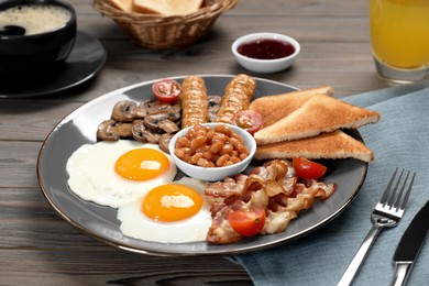 Photo of Plate of fried eggs, mushrooms, beans, tomatoes, bacon, sausages and toasts served on wooden table, closeup. Traditional English breakfast