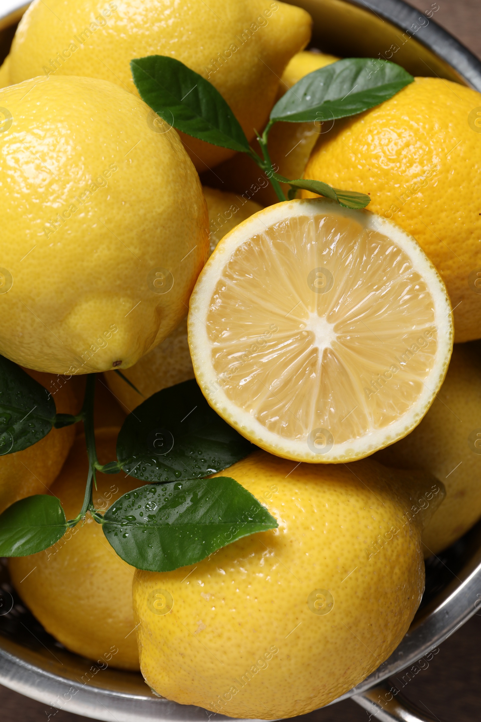 Photo of Fresh lemons and green leaves in colander, closeup