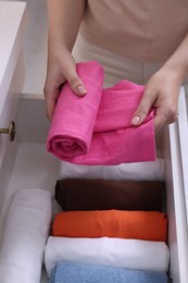 Photo of Woman putting rolled shirt into drawer, closeup. Organizing clothes
