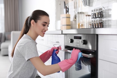 Photo of Young woman cleaning oven with rag in kitchen