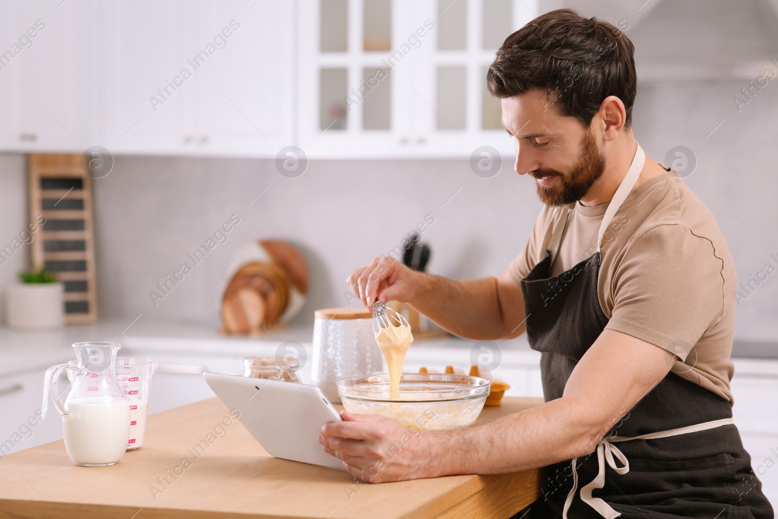 Photo of Man making dough while watching online cooking course via tablet in kitchen