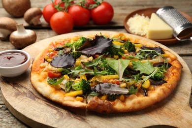 Photo of Delicious vegetarian pizza and ingredients on wooden table, closeup