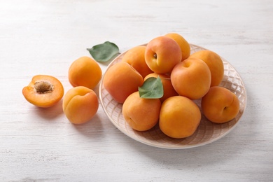 Plate of delicious ripe apricots on white wooden background