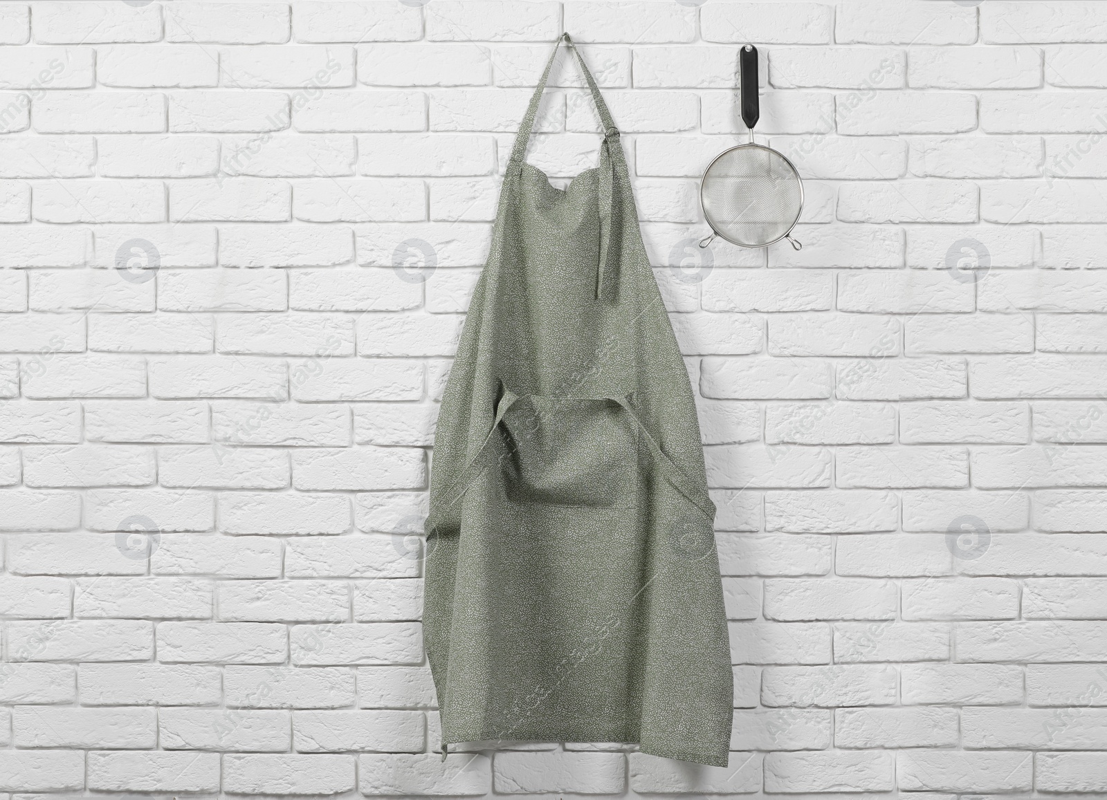 Photo of Clean kitchen apron with pattern and sieve on white brick wall