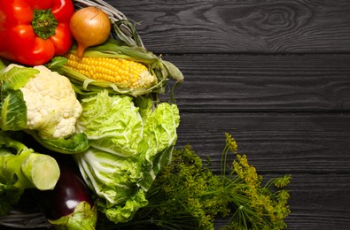 Photo of Different fresh vegetables in wicker basket on black wooden table, top view and space for text. Farmer harvesting
