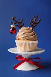 Tasty cupcake with chocolate reindeer antlers and Christmas bauble on blue background