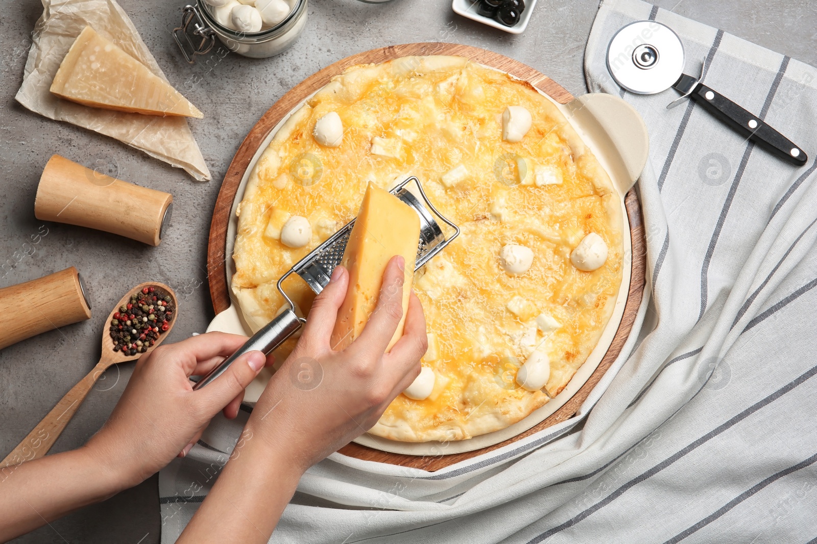 Photo of Woman grating cheese onto homemade pizza on table, top view