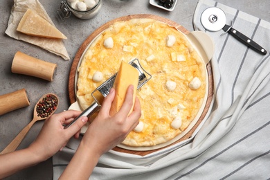 Woman grating cheese onto homemade pizza on table, top view