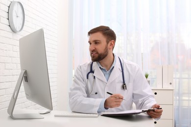 Pediatrician consulting patient online at table in clinic