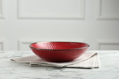 Photo of Beautiful red ceramic bowl and napkin on white marble table, space for text