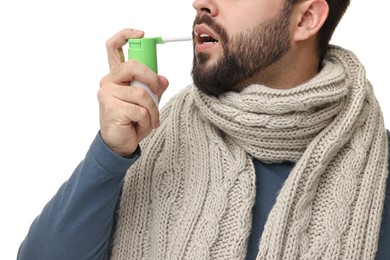 Young man with scarf using throat spray on white background, closeup