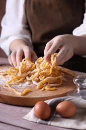 Photo of Woman making homemade pasta at wooden table, closeup