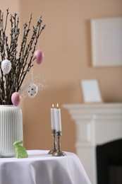 Pussy willow branches with festively decorated eggs, Easter bunny and candles on table indoors