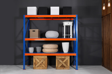 Photo of Metal shelving unit with wooden crates and different household stuff near black wall indoors