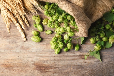 Photo of Fresh green hops and wheat spikes on wooden background, top view with space for text. Beer production