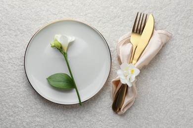 Photo of Stylish setting with cutlery, napkin, flowers and plate on light textured table, flat lay