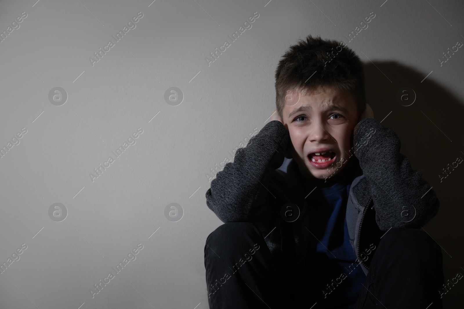 Photo of Scared little boy near beige wall, space for text. Domestic violence concept