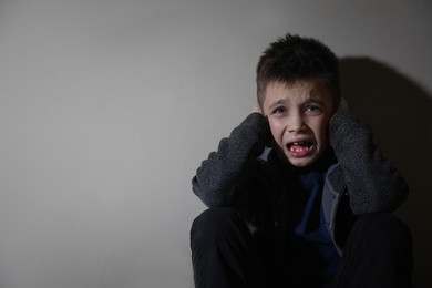 Photo of Scared little boy near beige wall, space for text. Domestic violence concept