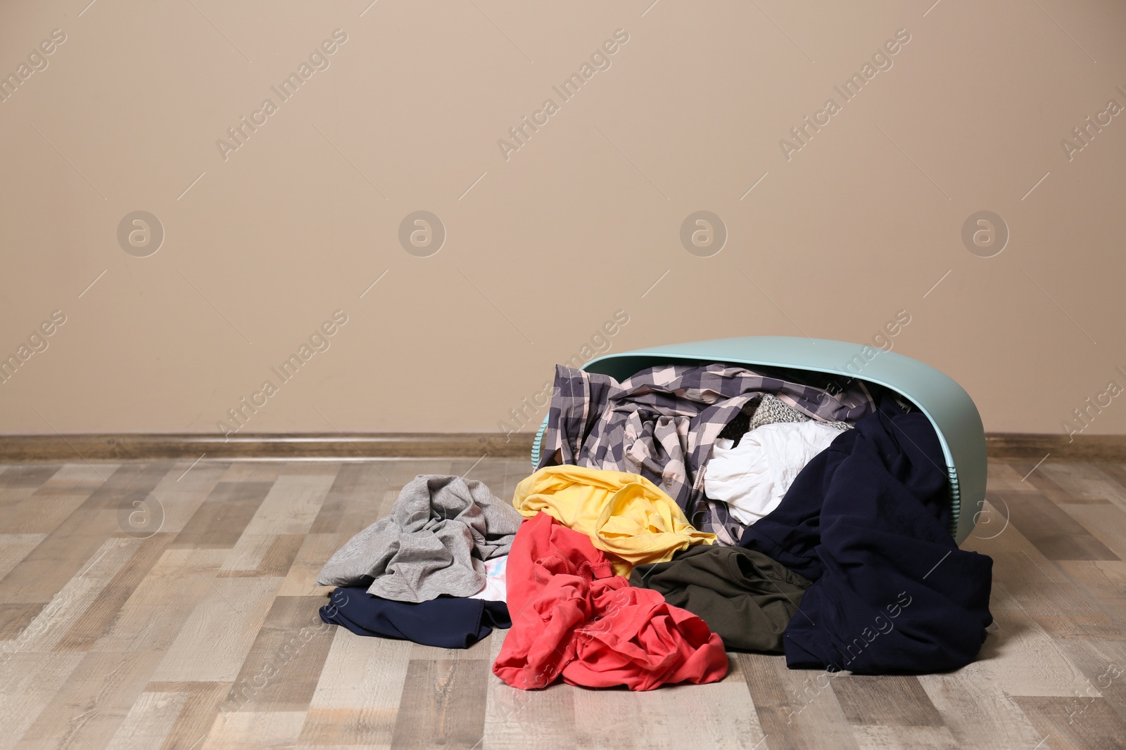 Photo of Dirty clothes scattered from laundry basket on floor indoors. Space for text