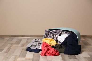 Photo of Dirty clothes scattered from laundry basket on floor indoors. Space for text