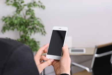 Photo of Woman holding mobile phone with blank screen in office, closeup. Space for text