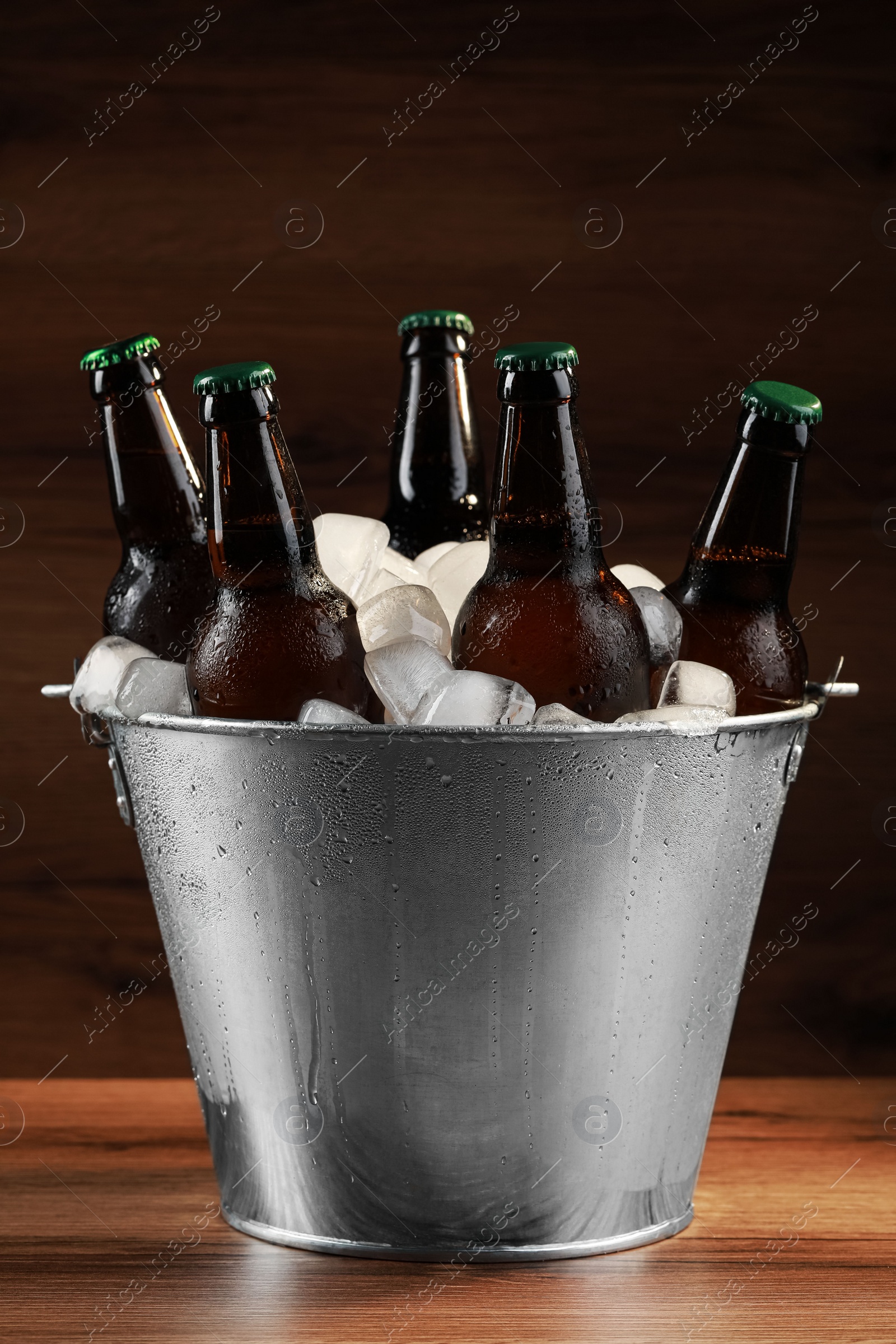 Photo of Metal bucket with bottles of beer and ice cubes on wooden table