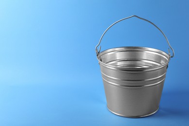 Photo of One shiny metal bucket on light blue background. Space for text