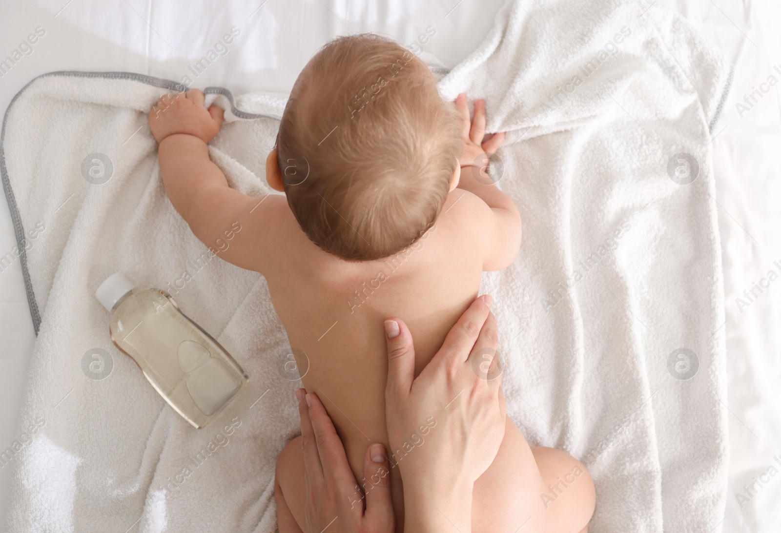 Photo of Mother massaging her baby with oil on towel after bathing, top view